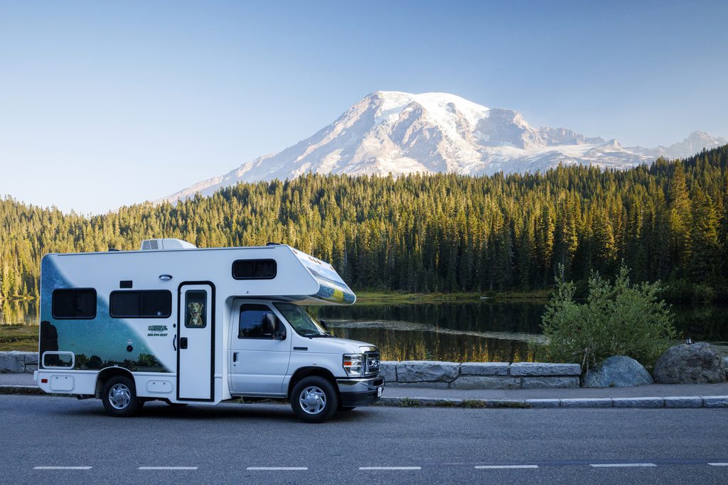 Scenic road trip featuring a Cruise America RV parked near a mountain lake and pine forest