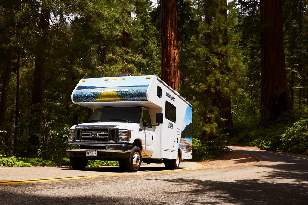 Scenic road trip featuring a Cruise America RV parked near a mountain lake and pine forest