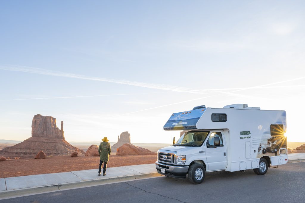 Traveler exploring red rock country with a Cruise America RV parked nearby